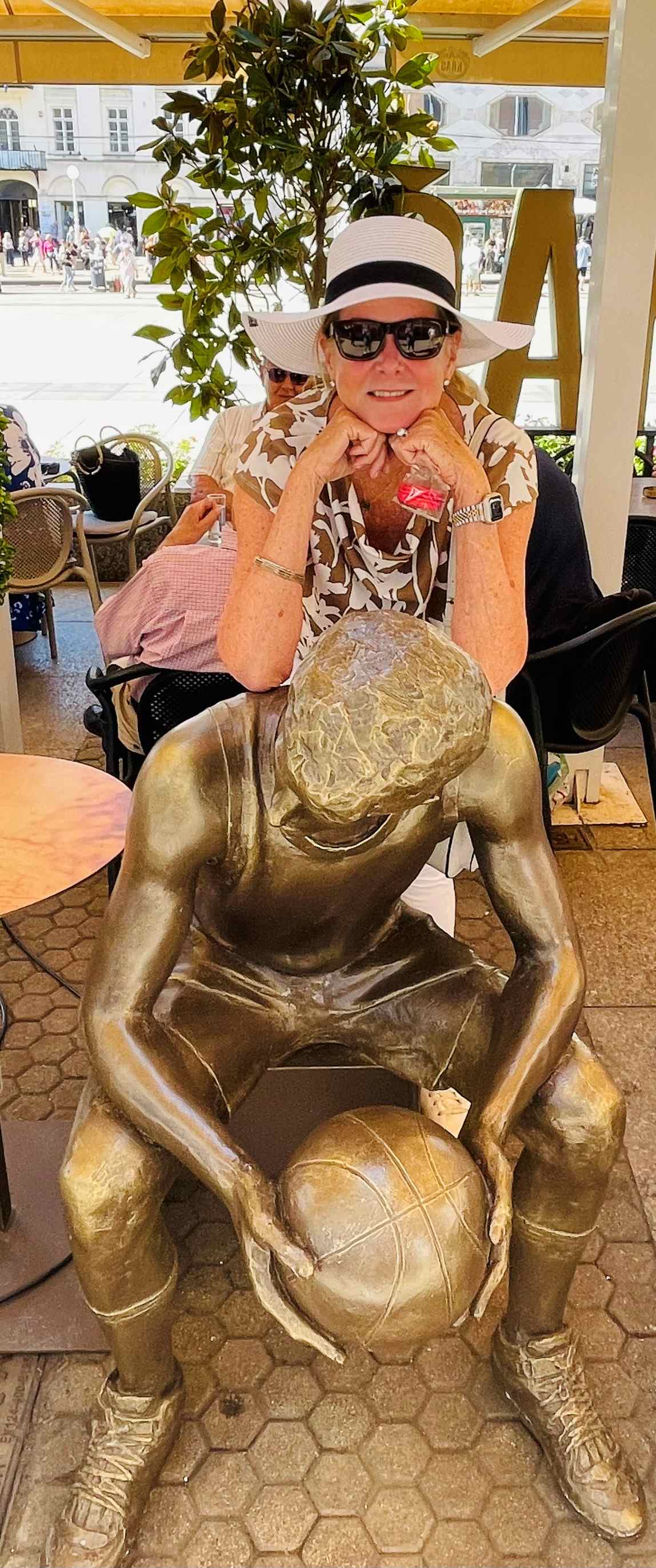 Robin in a white hat is leaning on a statue of Drazen Petrovic, a famous Croatian basketball star